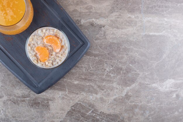 Porridge with two orange slices in a glass on a wooden tray next to orange juice, on the marble background.