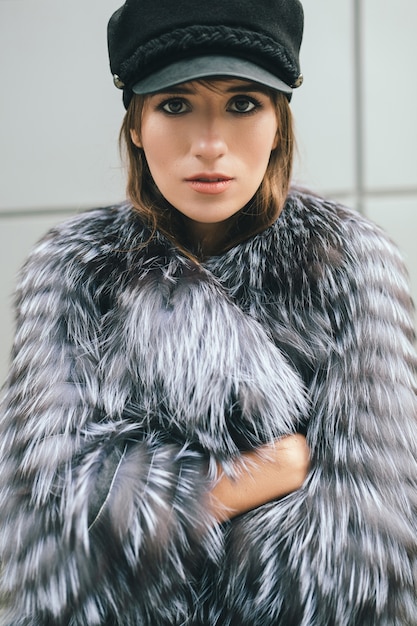 Free photo portrair of fashionable woman walking in city in warm fur coat, winter season, cold weather, wearing black cap, street fashion trend