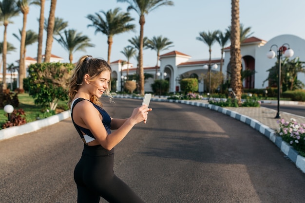 Portrait active happy sportswoman making selfie on street in tropical city. Sunny morning, cheerful mood, motivation, workout, smiling, healthy lifestyle, fitness, attractive model.