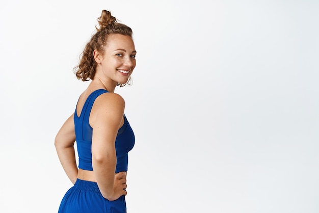 Free photo portrait of active and healthy sportswoman turn back looking behind put hands on waist and smiling with confidence doing exercises in sportswear white background