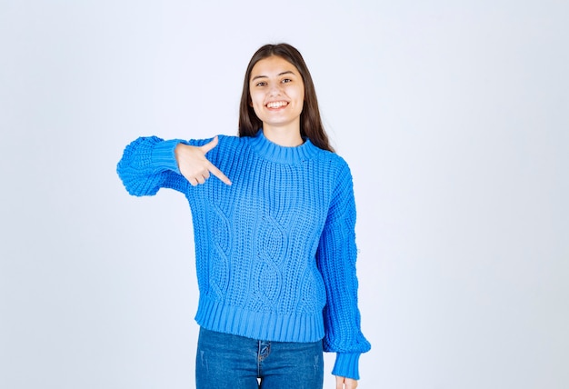 Portrait of adorable girl in blue sweater pointing downside on white.