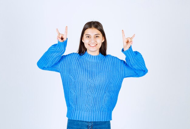 Portrait of adorable girl in blue sweater pointing on white.