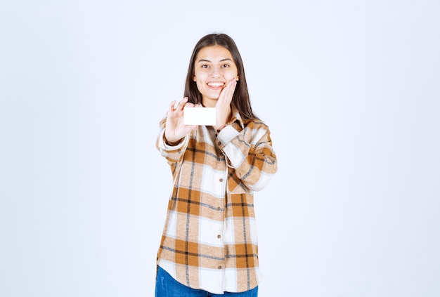 Foto gratuita ritratto di ragazza adorabile che mostra biglietto da visita sul muro bianco.