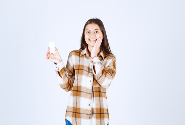 Portrait of adorable girl showing business card on white wall. 