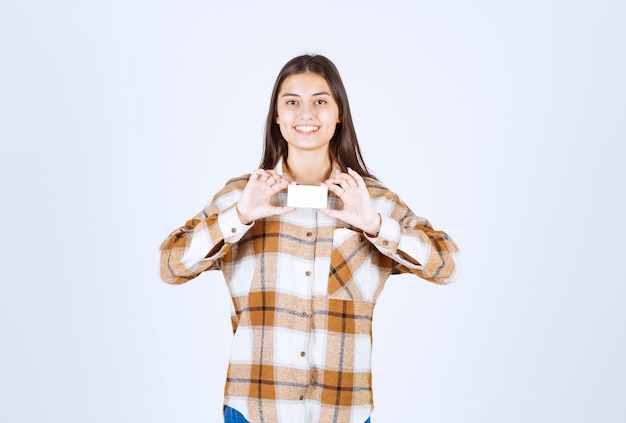 Portrait of adorable girl showing business card on white wall. 