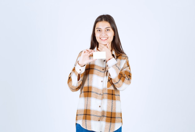 Portrait of adorable girl showing business card on white wall. 