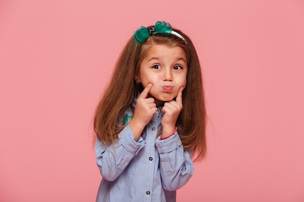 Portrait of adorable little girl with beautiful long auburn hair blowing up her cheeks touching face