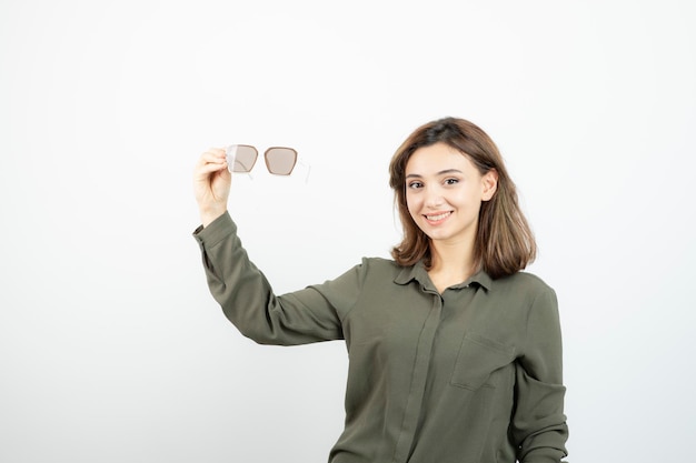 白の上に眼鏡を保持している愛らしい若い女性の肖像画。高品質の写真