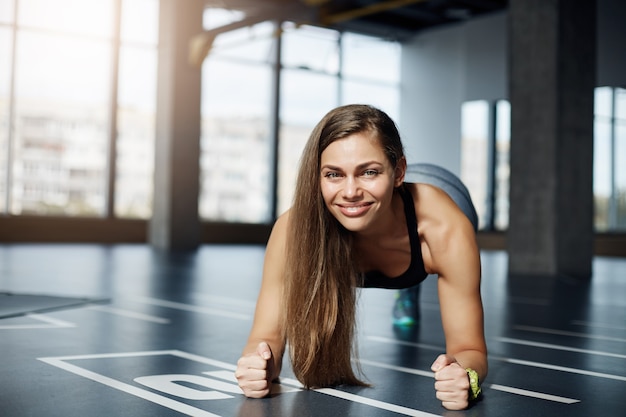 体育館の床で肘板運動をしている大人の美しい女性の肖像画。健康的なフィットネスボディのコンセプト。