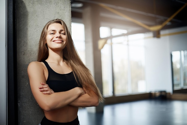 Портрет взрослой женщины-тренера по фитнесу, смотрящей в камеру с пустым тренажерным залом на заднем плане