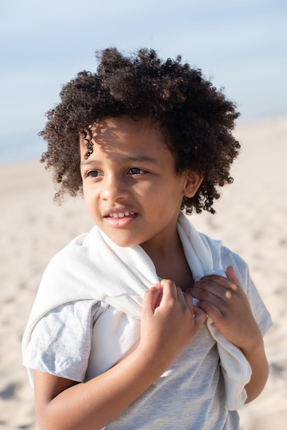 Portrait of African American child on beach alone. Female model with curly hair in T-shirt and sweatpants posing. Portrait, beauty concept