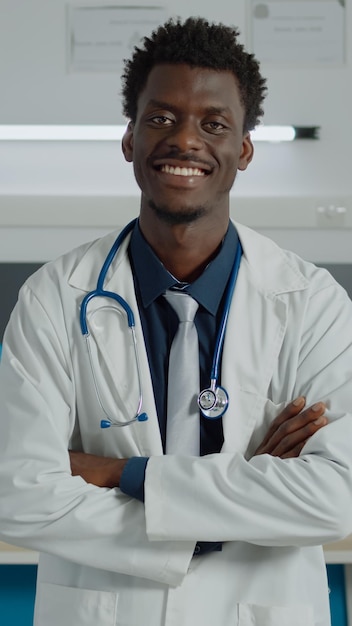상담을 위해 흰색 코트와 청진기를 입고 카메라를 바라보는 아프리카계 미국인 의사의 초상화. 의료 시설에서 장비를 들고 의사 사무실에서 웃고 있는 흑인