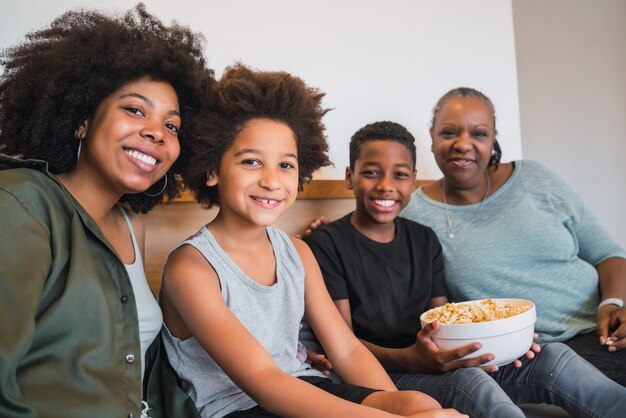 Портрет афро-американской бабушки, матери и детей, глядя в камеру и улыбаясь, сидя на диване у себя дома. Концепция семьи и образа жизни.