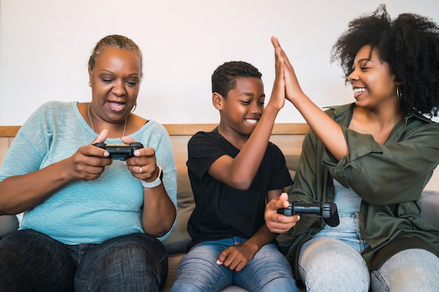 アフリカ系アメリカ人の祖母、母と息子が自宅で一緒にビデオゲームをプレイする肖像画。技術とライフスタイルのコンセプト。