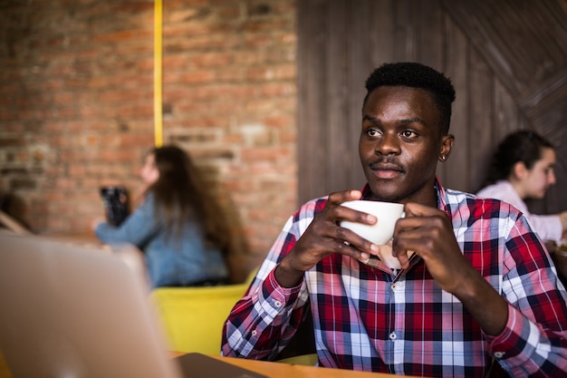 Портрет афро-американского человека, сидящего в кафе и работающего на ноутбуке.