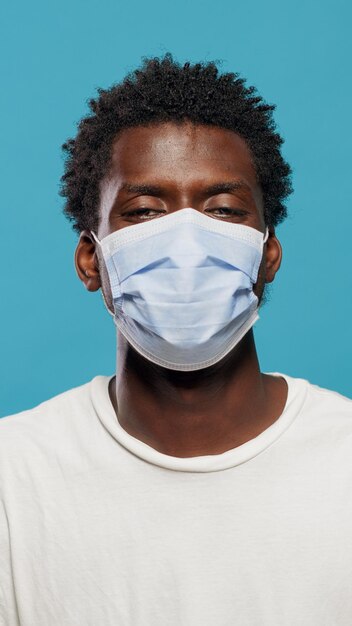 Портрет афро-американского мужчины в маске для защиты от коронавируса в студии. Закройте темнокожего человека, смотрящего в камеру, имея защитную маску на лице на фоне.