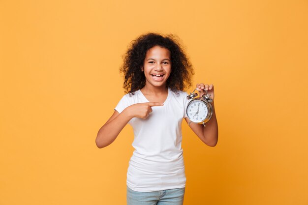 Portrait of a african girl pointing finger at alarm clock