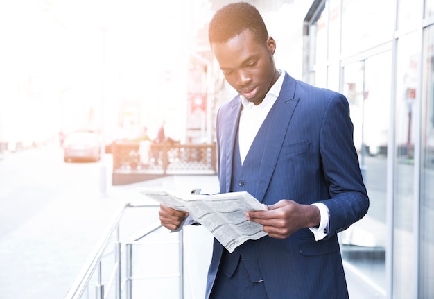 Portrait of an african young businessman standing outdoor the office reading the newspaper