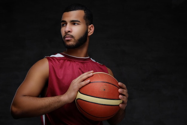 Free photo portrait of an afro-american sportsman. basketball player in sportswear with a ball on a dark background.