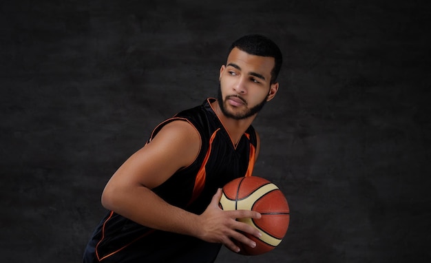 Portrait of an Afro-American sportsman. Basketball player in sportswear with a ball on a dark background.