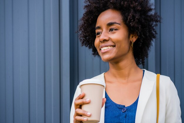 通りに屋外に立っている間コーヒーを保持しているアフロビジネス女性の肖像画