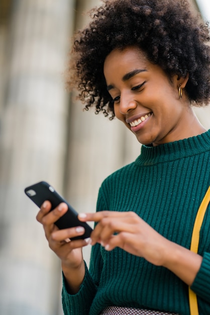 Portrait of afro business woman using her mobile phone while standing outdoors at the street