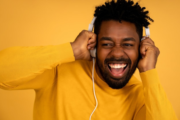 Портрет афро-человека, наслаждающегося прослушиванием музыки в наушниках, стоя на изолированном желтом фоне.