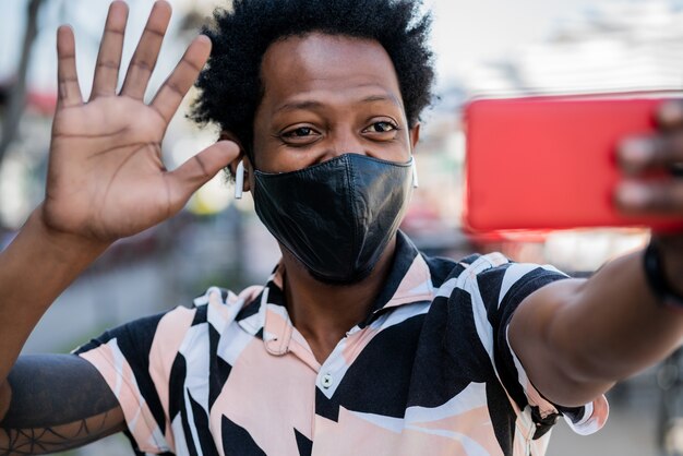 Portrait of afro tourist man doing video call on mobile phone while standing outdoors on the street. New normal life concept. Tourism concept.