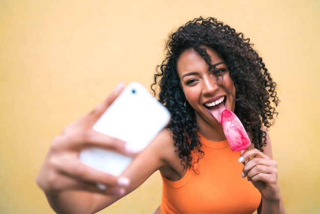 아이스크림을 먹는 동안 그녀의 mophile 전화로 selfies를 복용 아프리카 여자의 초상화. 기술 및 라이프 스타일 개념.
