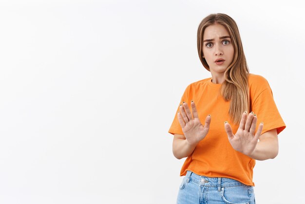 Portrait of alarmed, scared and reluctant young blonde woman, show stop, taboo gesture, rejecting, worried over person acting crazy