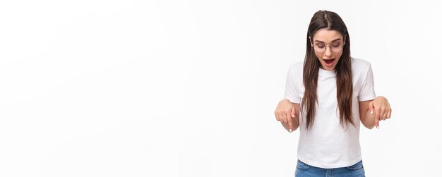 Portrait of amazed curious happy brunette woman in tshirt glasses looking and pointing down amused s