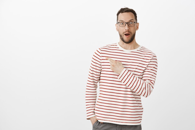 Free photo portrait of amazed grinning man in glasses, saying wow and pointing at upper left corner
