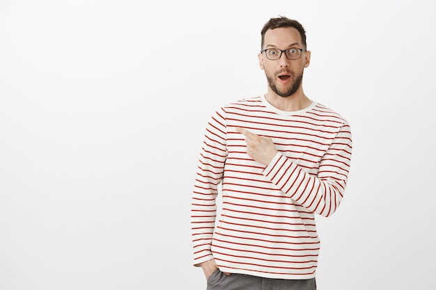 Portrait of amazed grinning man in glasses, saying wow and pointing at upper left corner