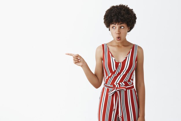 Portrait of amazed and impressed curious emotive woman gossiping about neighbour, pointing and looking left with folded lips, expressing curiosity and interest