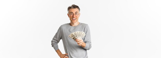 Portrait of amazed middleaged man in glasses and gray sweater holding money and smiling cheerful win