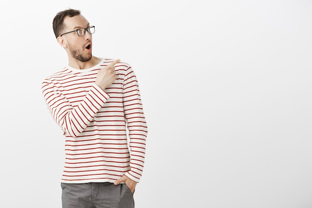 Portrait of amazed pleased cute guy in striped pullover and glasses