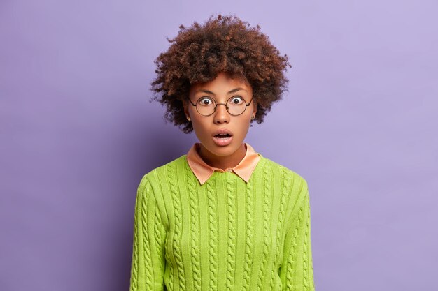 Portrait of amazed speechless woman with curly hair stares shocked impressed keeps mouth wide opened