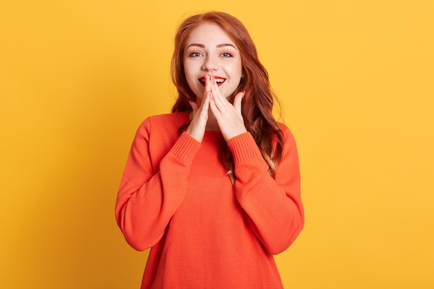 Portrait of amazed young woman posing with excited facial expression isolated, keeping hands on her mouth