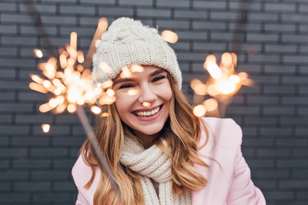 Ritratto di incredibile modello femminile guardando la luce del bengala con un sorriso. ridendo bella donna in cappello lavorato a maglia per celebrare il nuovo anno.