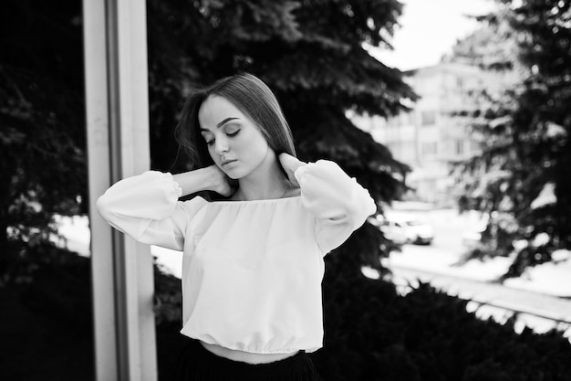 Portrait of an amazing woman in white blouse and wide black pants posing with pine trees on the background Black and white photo