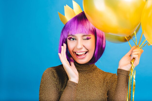 Портрет удивительной молодой женщины празднует карнавал, большую вечеринку. Стрижка фиолетовых волос, макияж розовых мишур, золотая корона, воздушные шары. Праздничное настроение, счастье, проявление позитива.