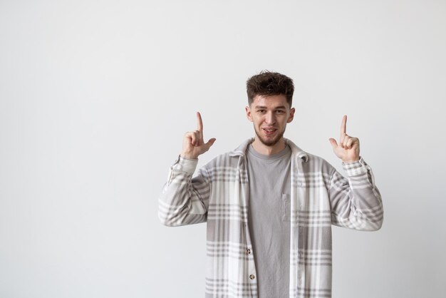 Portrait of an amused excited man standing and pointing two fingers up at copy space while looking at camera isolated over white background