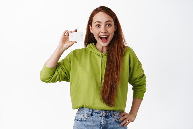 Portrait of amused happy ginger girl, showing small tiny size, rejoice of awesome little thing, standing in casual clothes against white background