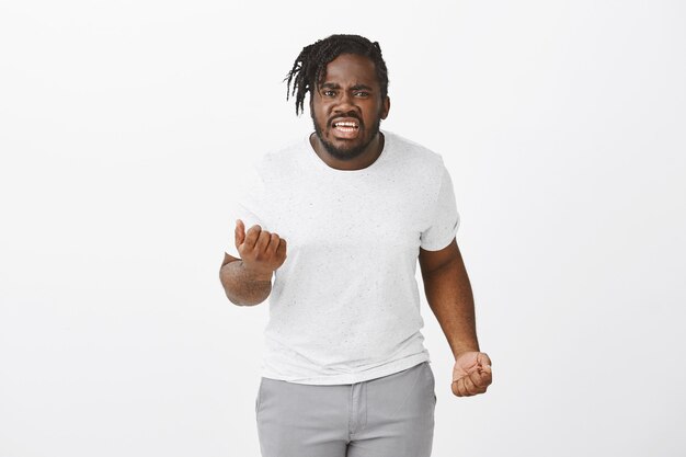 Portrait of angry guy with braids posing against the white wall