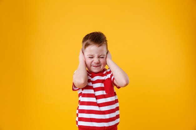 Portrait of an angry unhappy irritated little boy covering ears