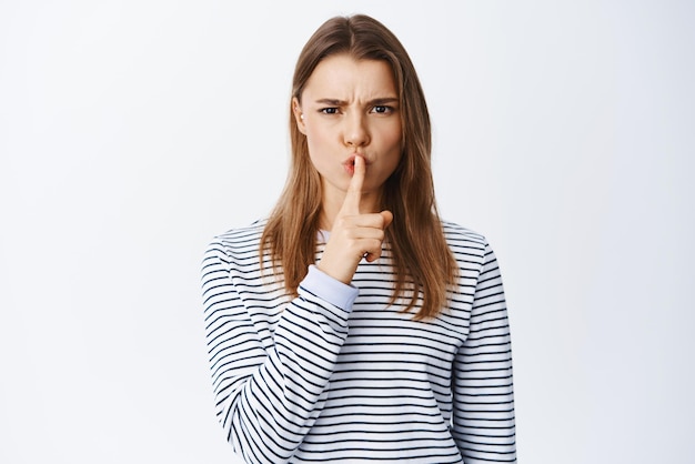 Portrait of angry woman frowning shushing at camera and tell to be quiet need silence scolding someone for being loud standing against white background