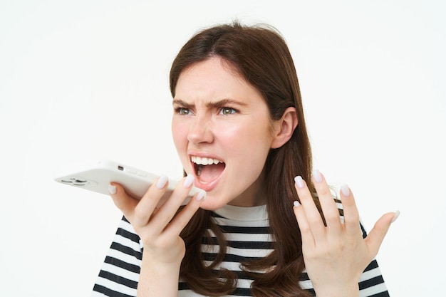 Portrait of angry woman shouting at smartphone speakerphone recording voice message with annoyed