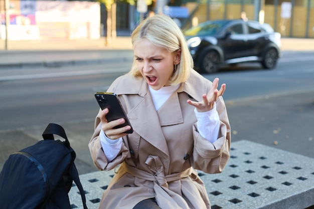 Foto gratuita ritratto di una giovane donna arrabbiata che urla al suo cellulare in frustrazione essendo indignata seduta su