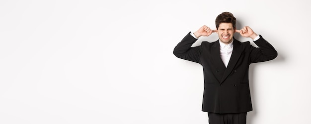 Free photo portrait of annoyed and bothered businessman in black suit shut ears feeling uncomfortable complaining loud noise standing against white background