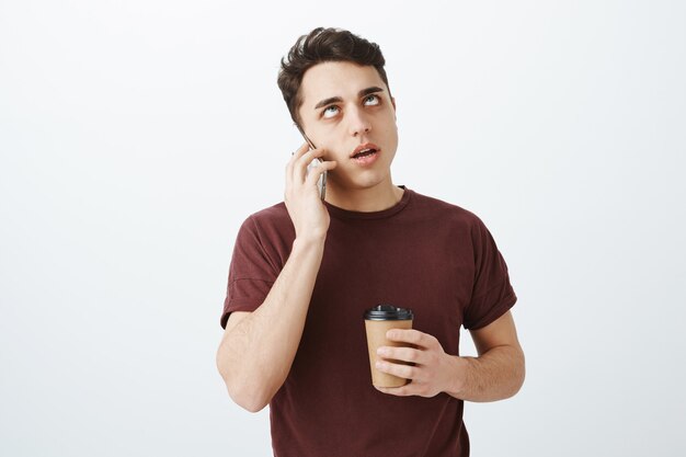 Portrait of annoyed pissed european guy in red t-shirt talking by phone